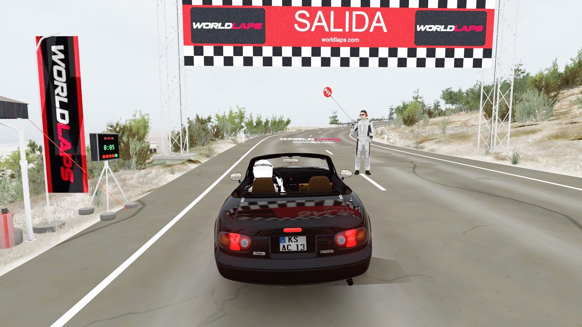 Assetto Corsa screenshot at the start of the Dos Aguas stage: the car under the SALIDA (start) gantry, the marshal with the flag and the road turning into the bend through low scrub.