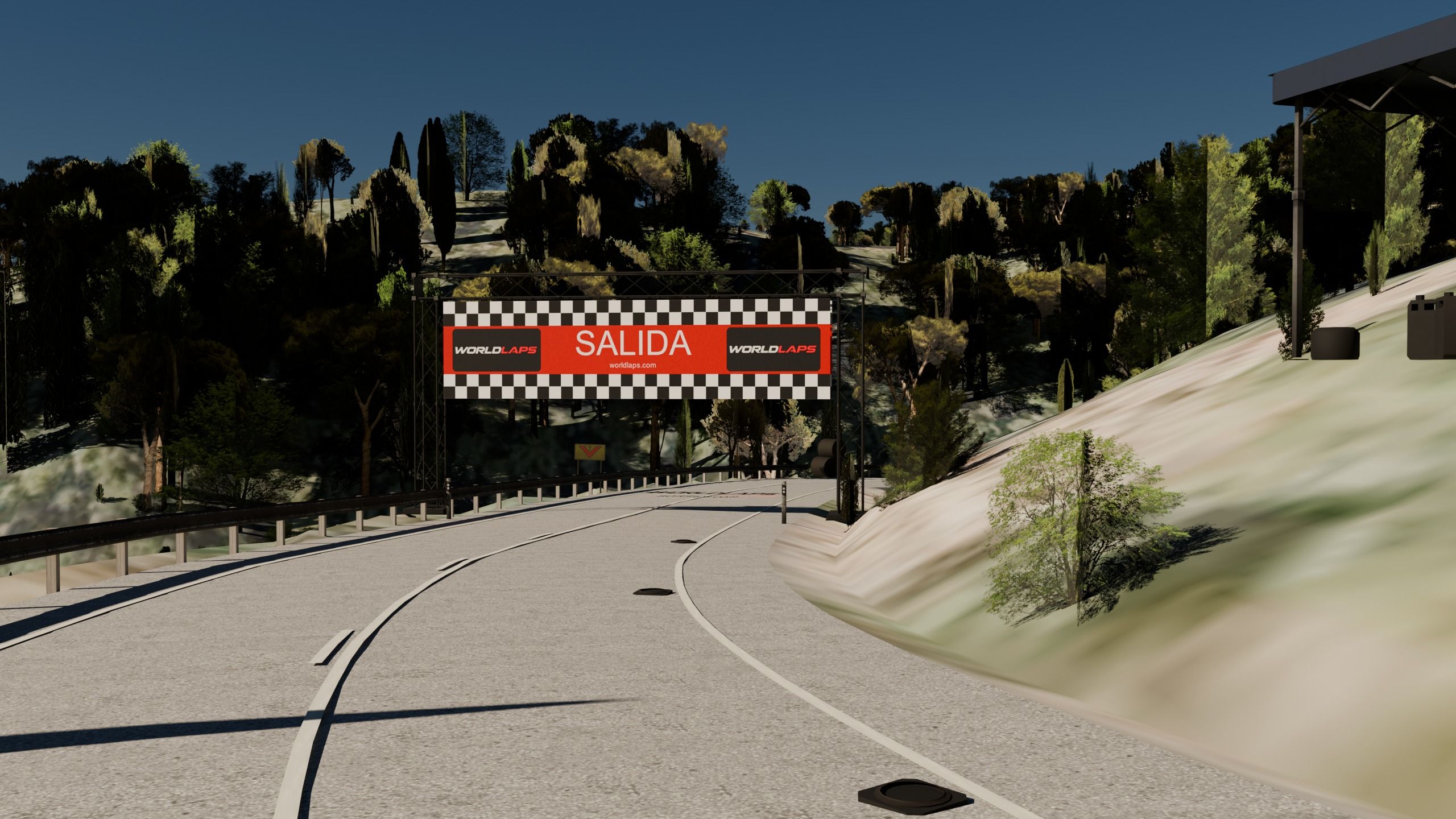 Pórtico de SALIDA con la marca Worldlaps sobre la carretera de montaña, con la curva, el quitamiedos y los pinos.